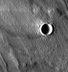 Grooved terrain (interrupted by an impact crater) overlies lava flows near the giant shield volcano Arsia Mons. The parallel ridges may be moraines, deposits of sand and rocks left by a cold-based glacier on the side of the volcano. (NASA/JPL-Caltech/Arizona State University)